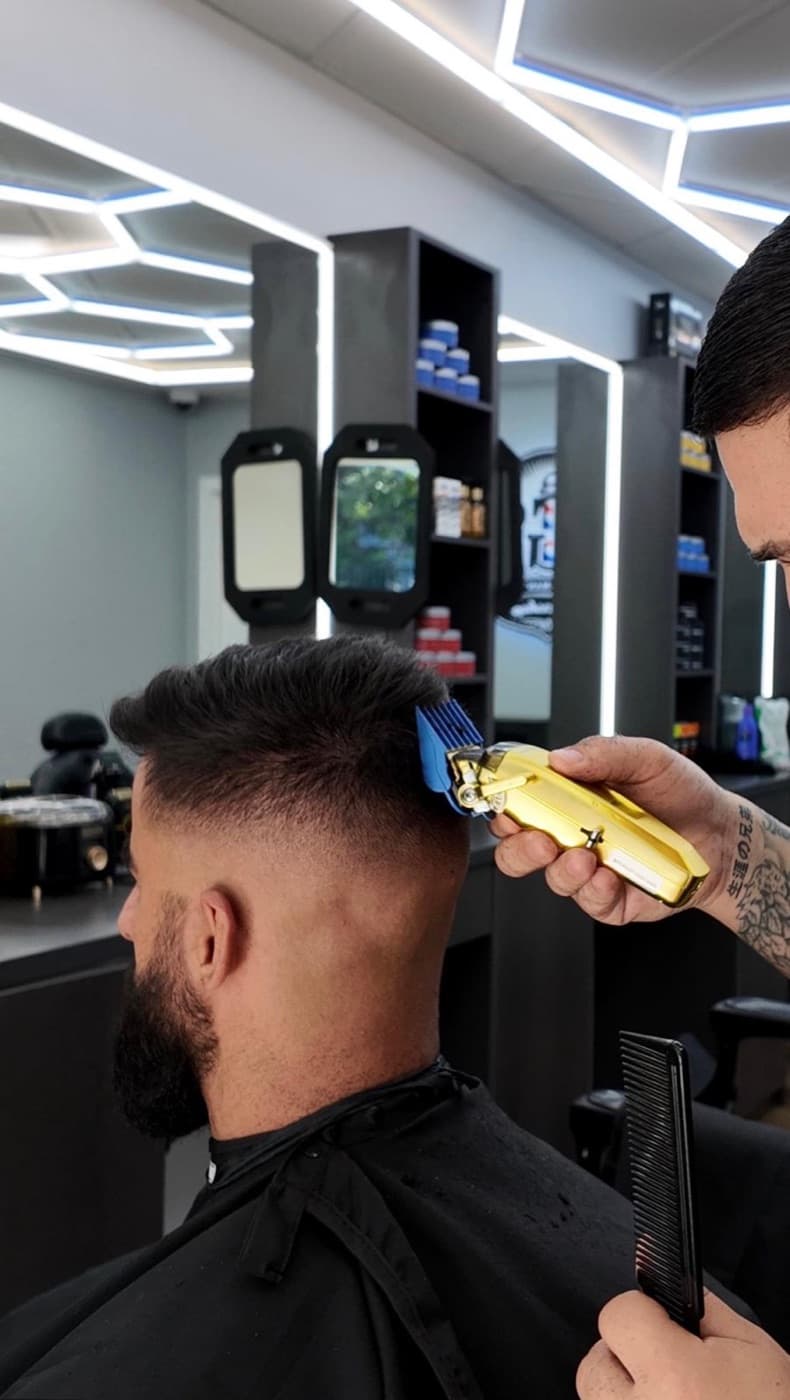 A TGS barber blending a mid fade with clippers, comb in hand