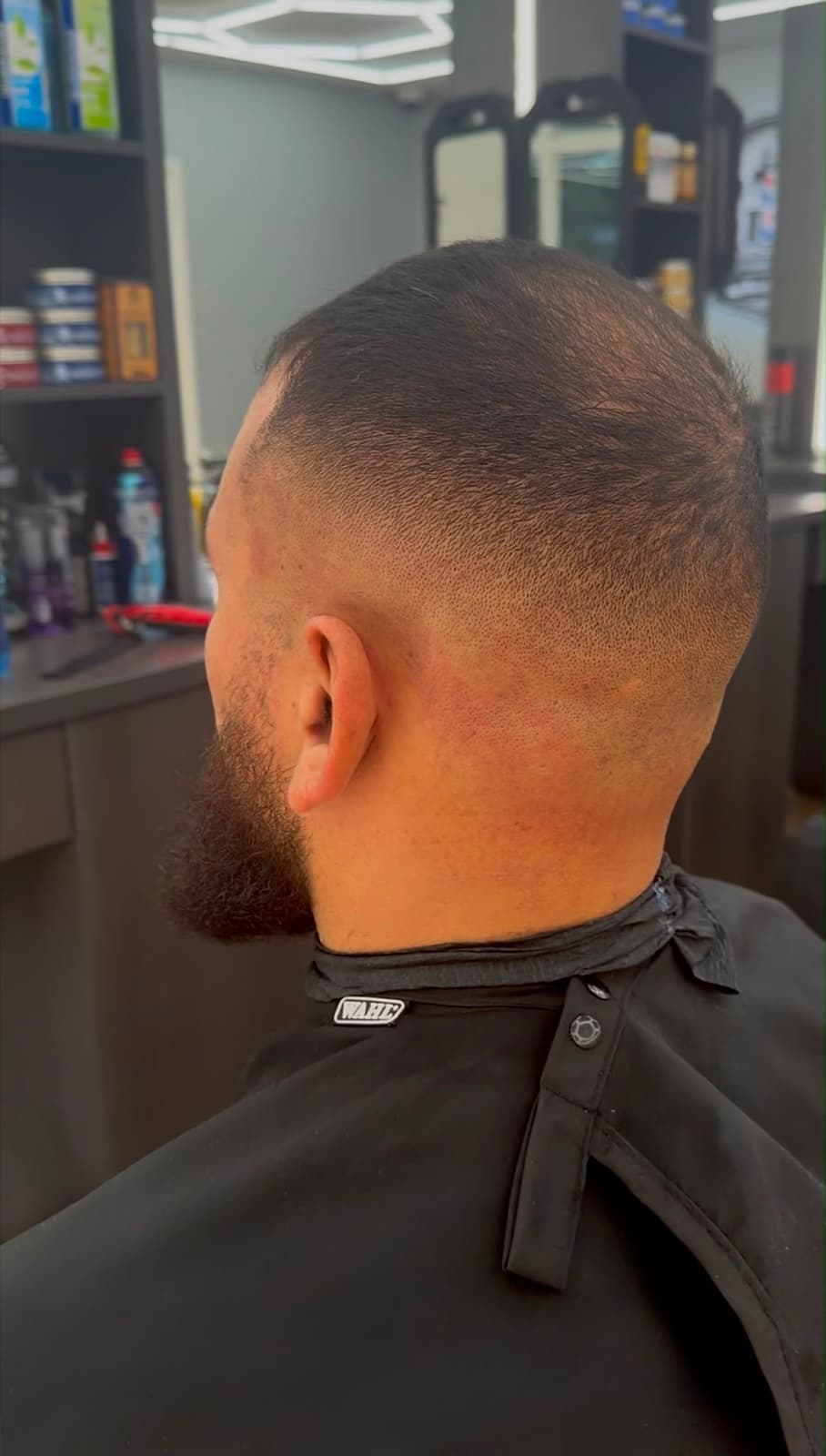 Close-up of a skin fade blended into a full beard, seen from behind