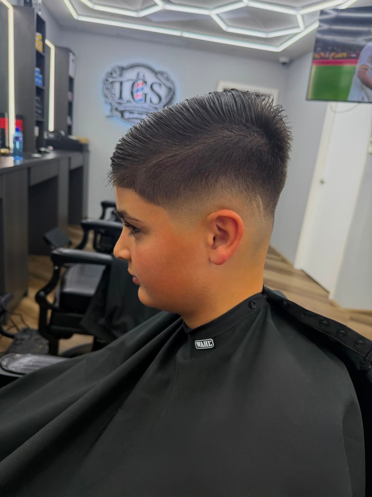A young client's textured fade with spiked, styled top, the TGS sign behind