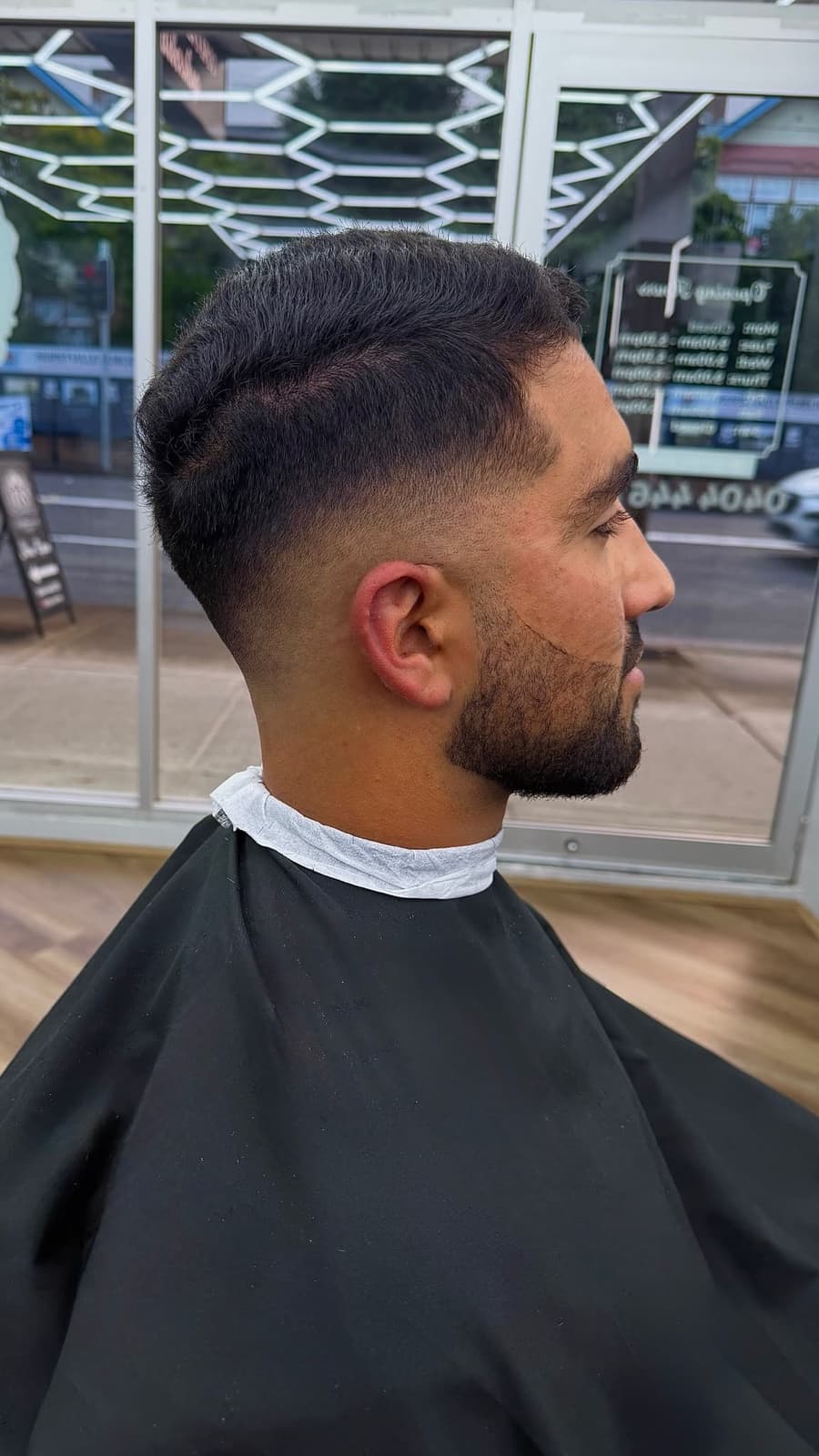 Profile view of a fade and beard by the shop's front window